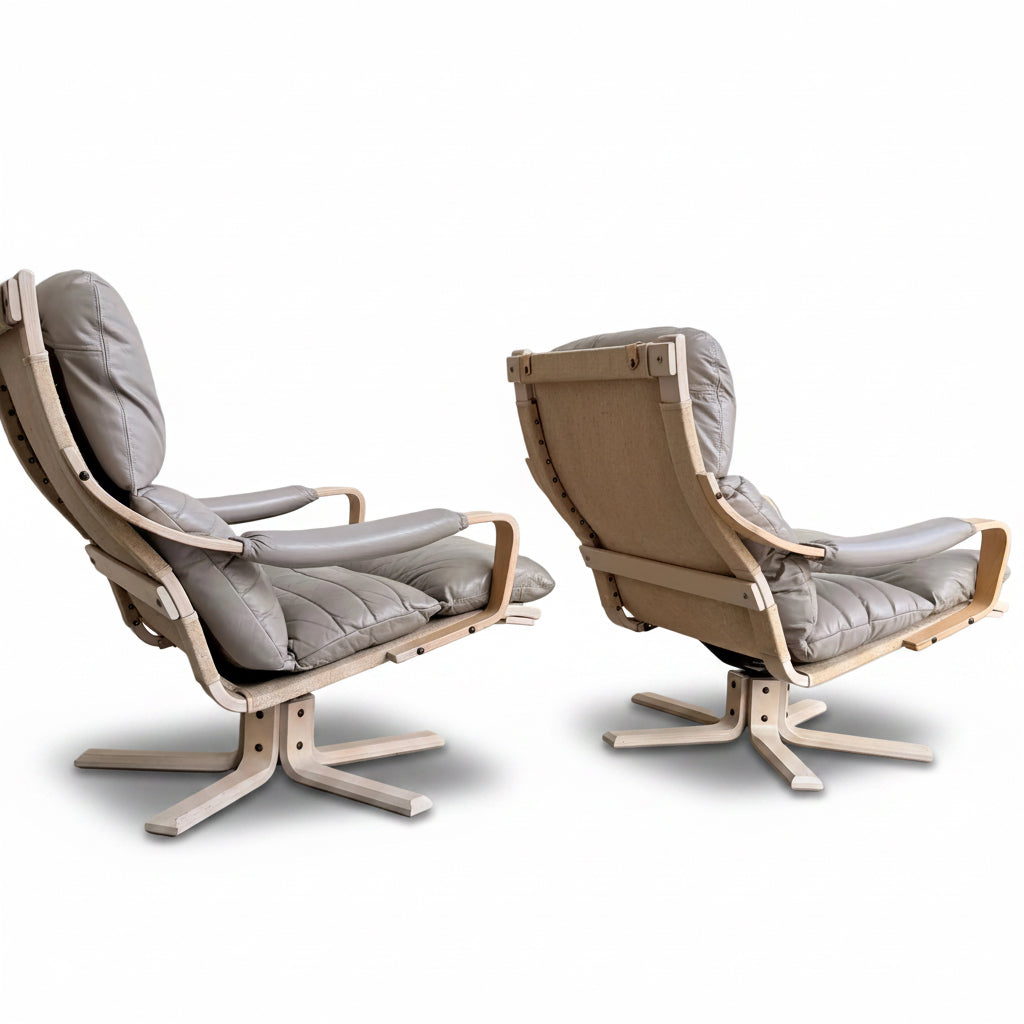 A Pair of Tessa Ferrara Swivel Armchairs (Revive) with light wood frames and tufted gray cushions are set on a concrete floor against a plain wall, angled to showcase their mid-century Australian-inspired design.