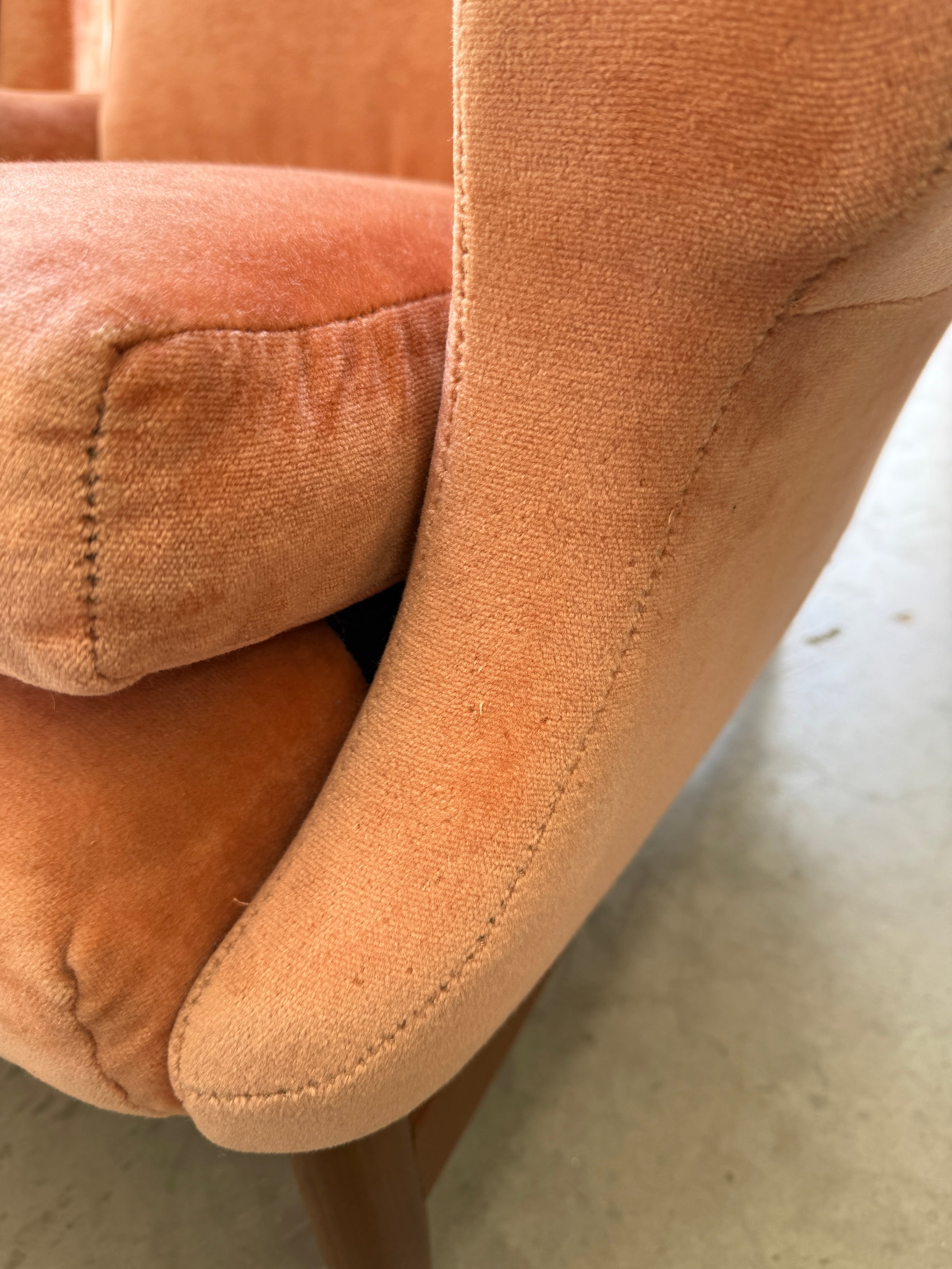 Close-up of a Mid-Century High-Back Wingback Armchair in dusty pink velvet with a blackwood frame, showing the armrest, seat cushion, and wooden leg. Visible texture and light wear reflect its vintage Rediscover character. Priced individually.