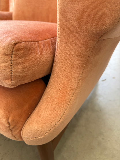 Close-up of a Mid-Century High-Back Wingback Armchair in dusty pink velvet with a blackwood frame, showing the armrest, seat cushion, and wooden leg. Visible texture and light wear reflect its vintage Rediscover character. Priced individually.
