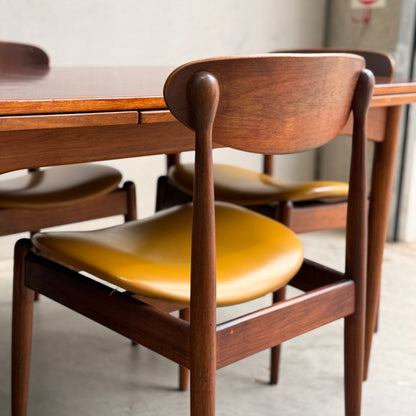 A close-up of the 107 Parker Matchstick chairs set of 4—COMING SOON—features curved backs and mustard yellow seats around a wooden table, showcasing striking vintage Australian design on a concrete floor.