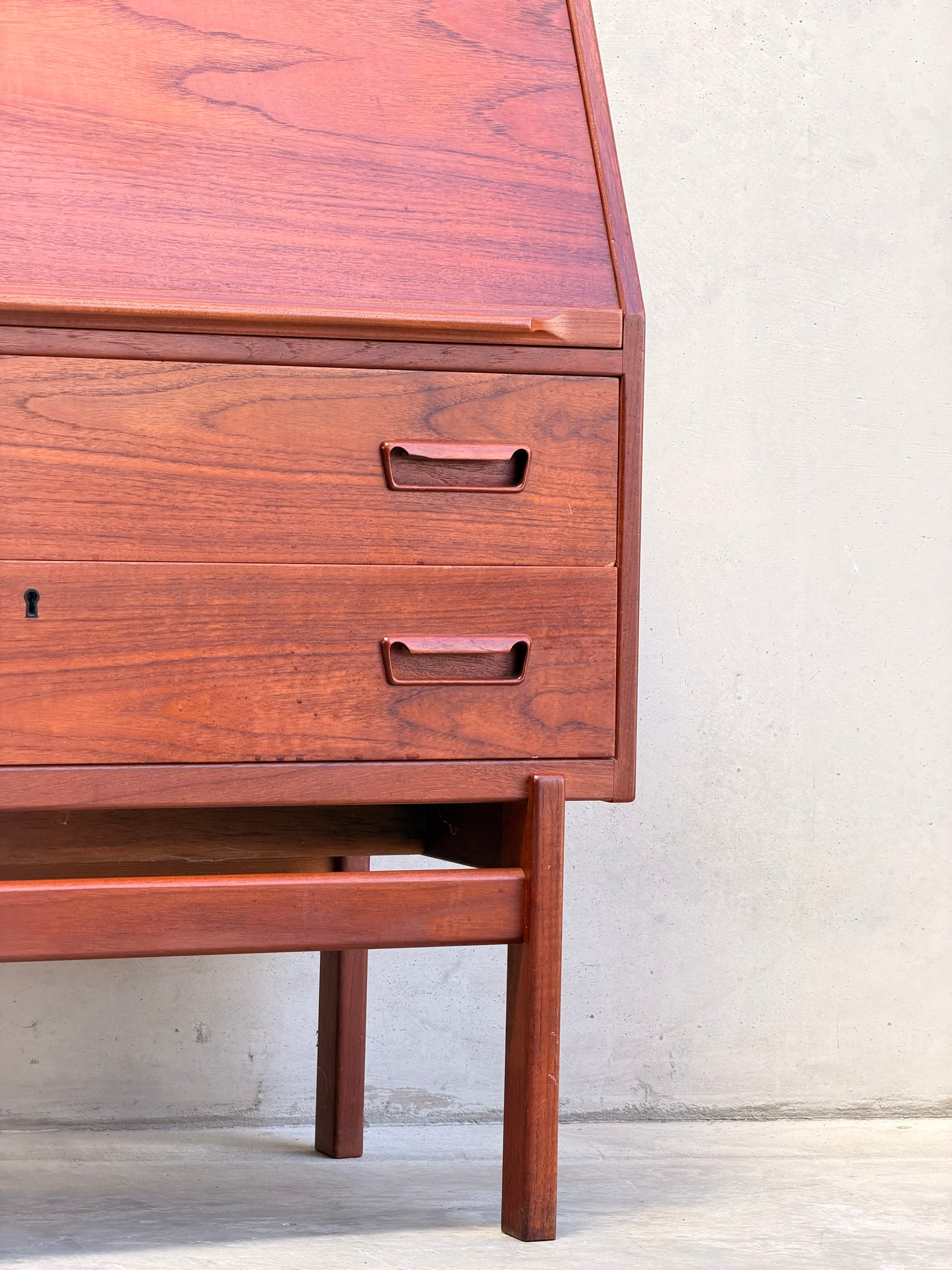 Close-up of a Mid Century Modern Danish Arne Wahl Iversen Model 68 Teak Secretary Desk by Vinde Møbelfabrik, featuring two drawers, an angled lid, and minimalist handles in classic mid-century style against a light wall and concrete floor.