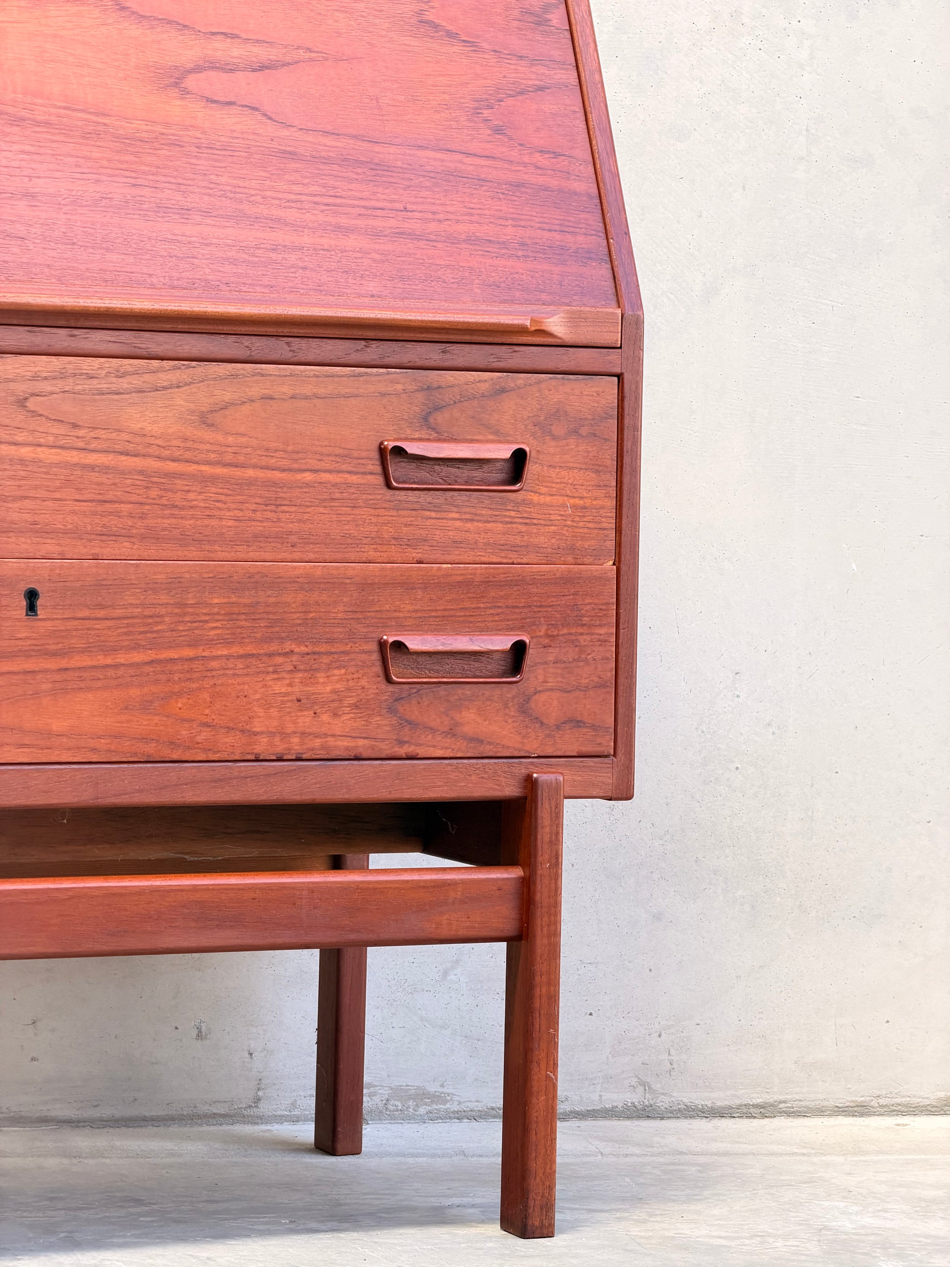 Close-up of a Mid Century Modern Danish Arne Wahl Iversen Model 68 Teak Secretary Desk by Vinde Møbelfabrik, featuring two drawers, an angled lid, and minimalist handles in classic mid-century style against a light wall and concrete floor.