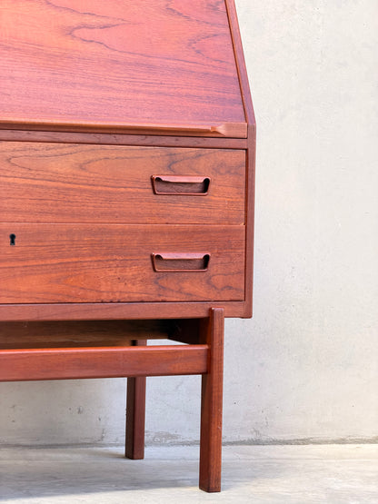 Close-up of a Mid Century Modern Danish Arne Wahl Iversen Model 68 Teak Secretary Desk by Vinde Møbelfabrik, featuring two drawers, an angled lid, and minimalist handles in classic mid-century style against a light wall and concrete floor.