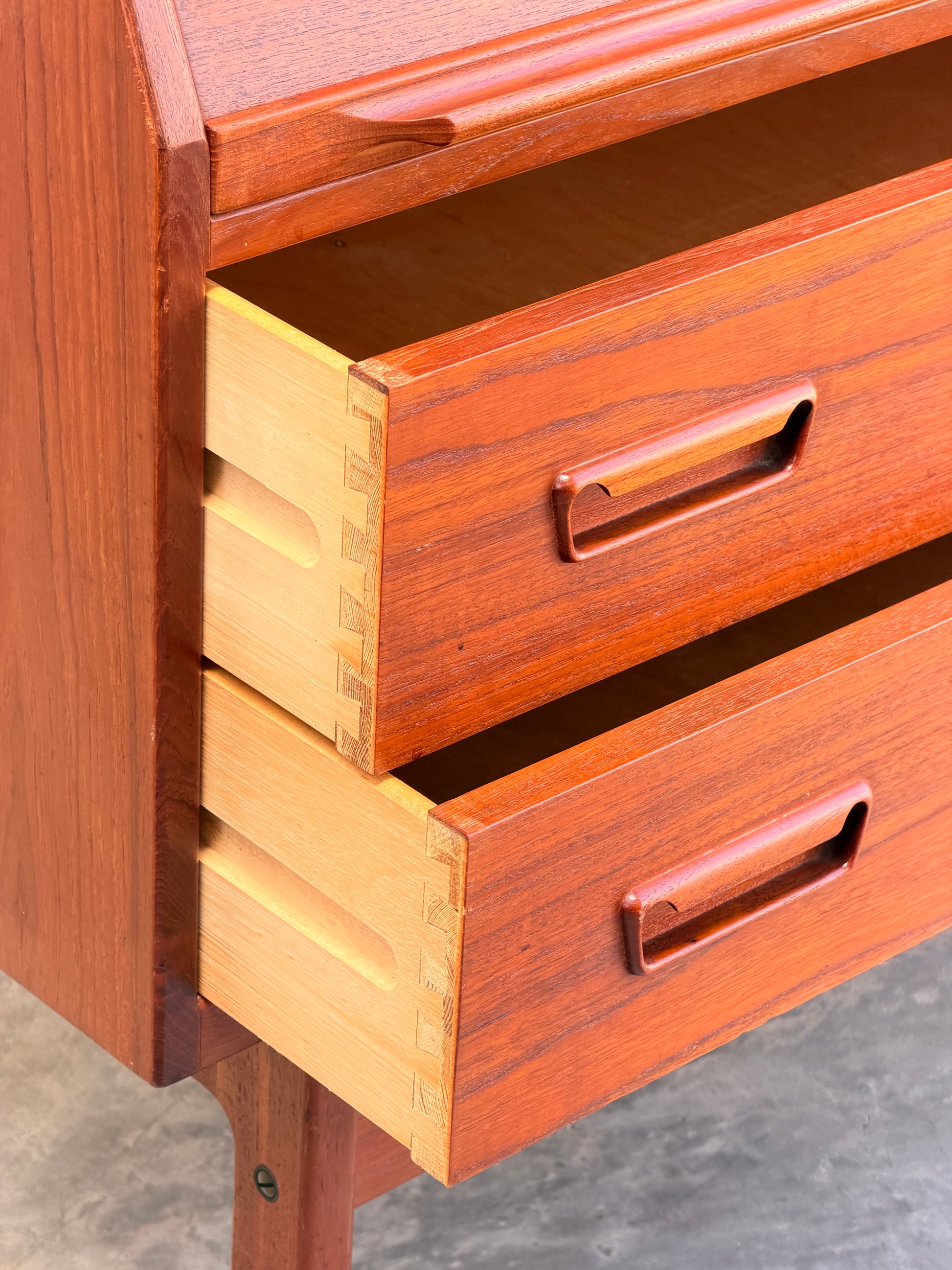 Close-up of the Mid Century Modern Danish Arne Wahl Iversen Model 68 Teak Secretary Desk by Vinde Møbelfabrik, featuring two open drawers with dovetail joints and integrated handles, set on a smooth gray floor.