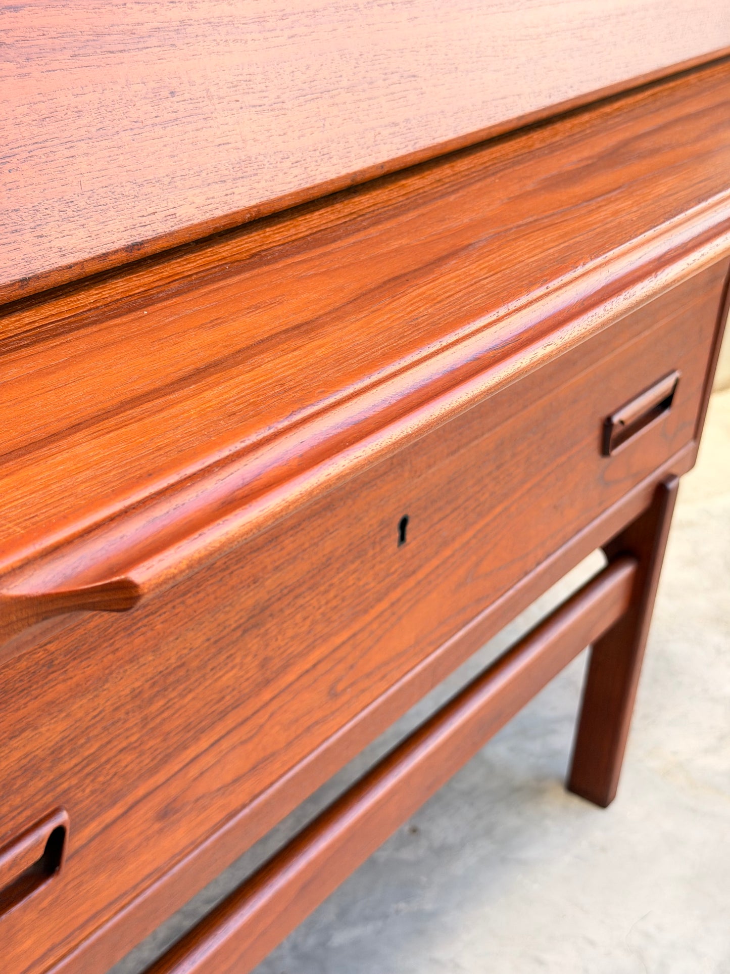 Close-up of a Mid Century Modern Danish Arne Wahl Iversen Model 68 Teak Secretary Desk by Vinde Møbelfabrik, featuring smooth teak finish, visible wood grain, minimalist handles, and sleek legs over a concrete floor.