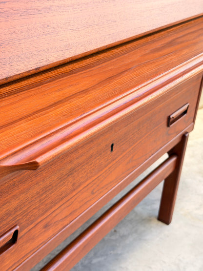 Close-up of a Mid Century Modern Danish Arne Wahl Iversen Model 68 Teak Secretary Desk by Vinde Møbelfabrik, featuring smooth teak finish, visible wood grain, minimalist handles, and sleek legs over a concrete floor.