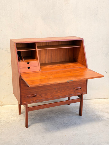 A Mid Century Modern Danish Arne Wahl Iversen Model 68 Teak Secretary Desk by Vinde Møbelfabrik, featuring open cubbies, small drawers, and a drop-down writing surface, sits against a plain light-colored wall and concrete floor.