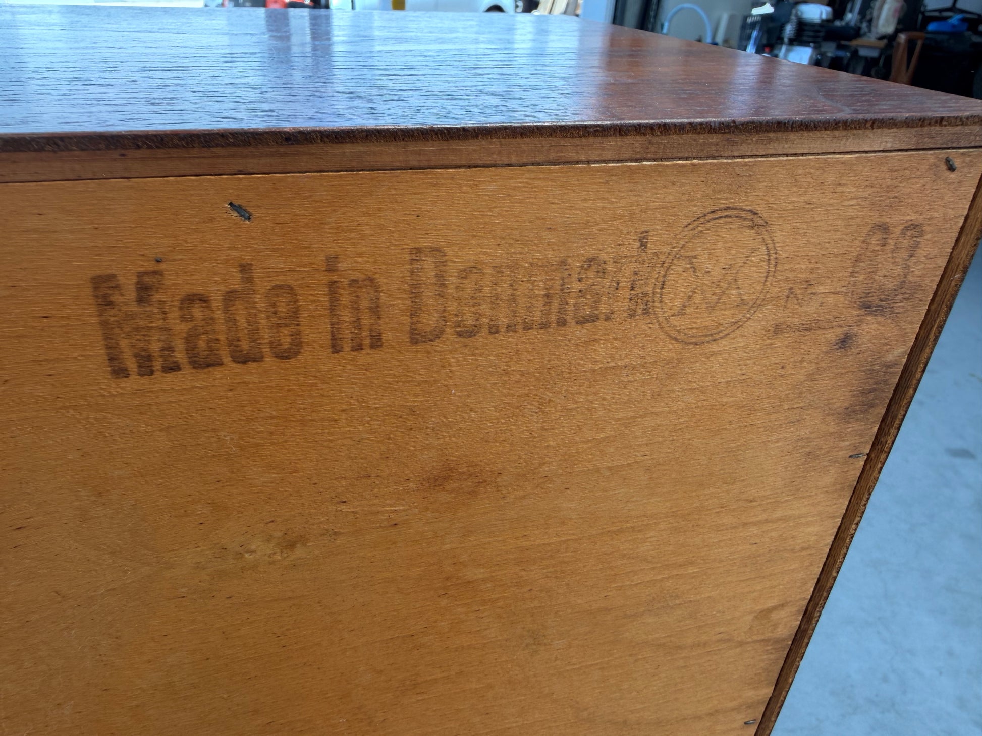A close-up of the Mid Century Modern Danish Arne Wahl Iversen Model 68 Teak Secretary Desk by Vinde Møbelfabrik, stamped "Made in Denmark," showcases its timeless design and heritage in a workshop setting.