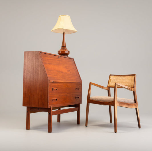A Mid Century Modern Danish Arne Wahl Iversen Model 68 Teak Secretary Desk by Vinde Møbelfabrik stands beside a wooden chair with woven cane back and cushioned seat, both set against a plain background.