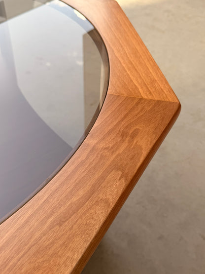 Close-up of the Octagonal Mid Century Coffee Table by Kalmar Furniture, featuring a smooth hardwood frame with a warm finish and smoked glass top—a stylish revival with magazine rack, blending classic mid-century elegance.