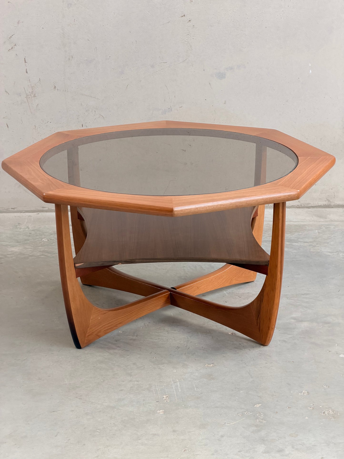 An octagonal hardwood Kalmar Furniture coffee table with smoked glass top and integrated magazine rack (Revive), set against a concrete backdrop—an elegant statement of mid-century modern Australian design.