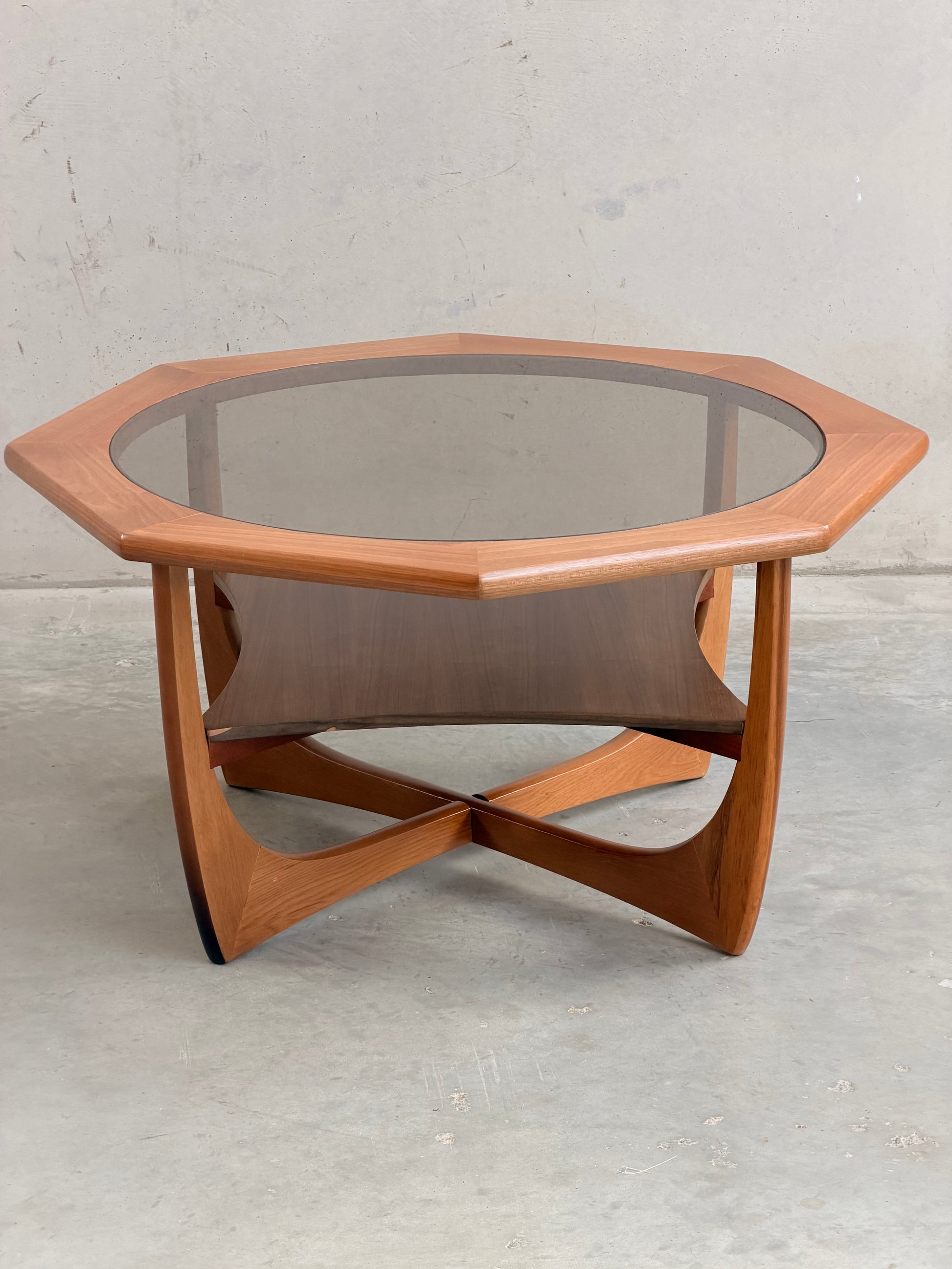 An octagonal hardwood Kalmar Furniture coffee table with smoked glass top and integrated magazine rack (Revive), set against a concrete backdrop—an elegant statement of mid-century modern Australian design.