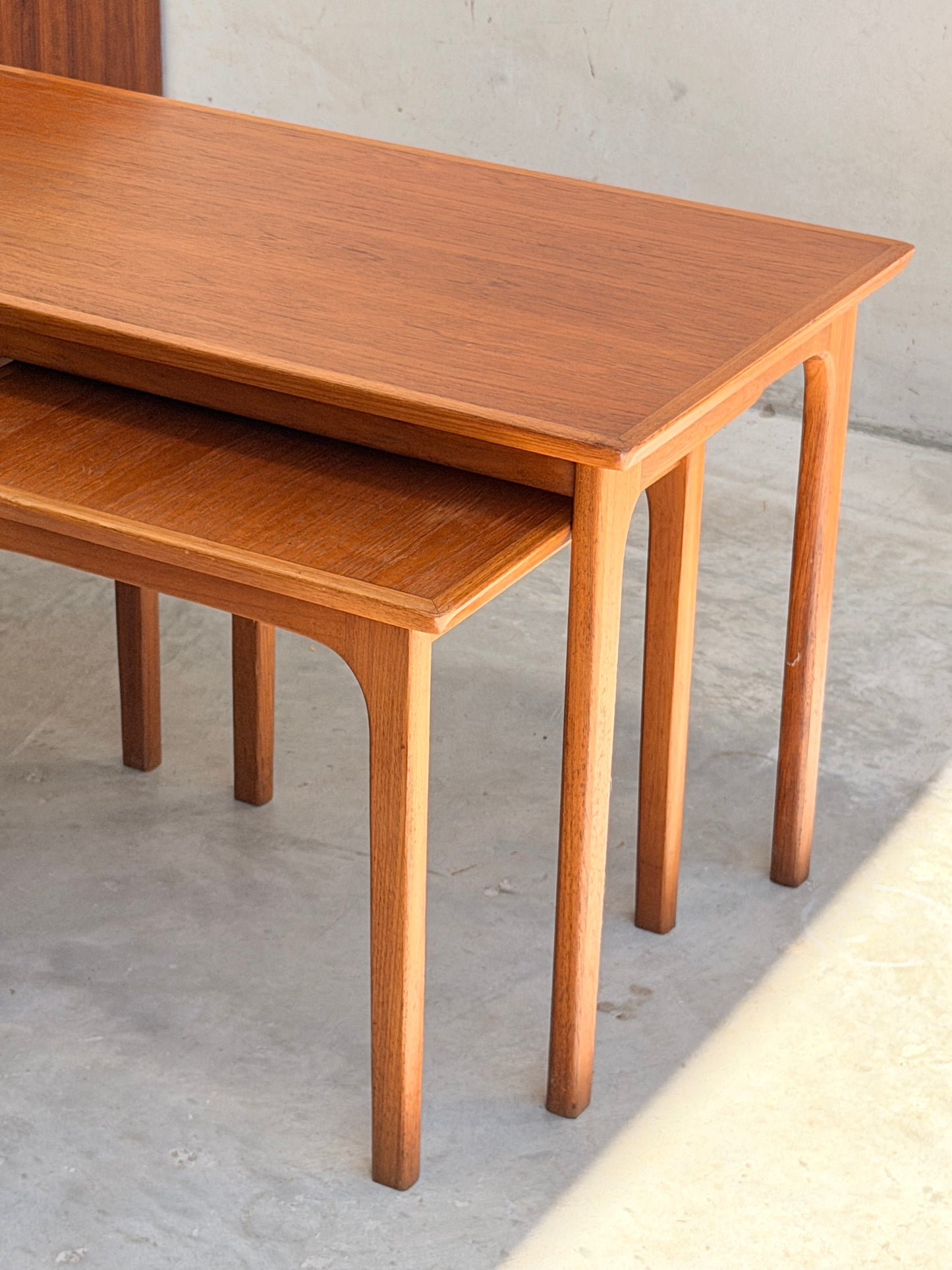 Two Classic Australian-Made Noblett Mid-Century Teak Nesting Tables (circa 1970s, Revive) are stacked on a light floor. Featuring Scandinavian design, they showcase a warm teak finish, clean lines, and gently curved legs.