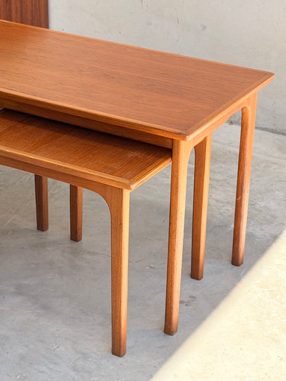 Two Classic Australian-Made Noblett Mid-Century Teak Nesting Tables (circa 1970s, Revive) are stacked on a light floor. Featuring Scandinavian design, they showcase a warm teak finish, clean lines, and gently curved legs.