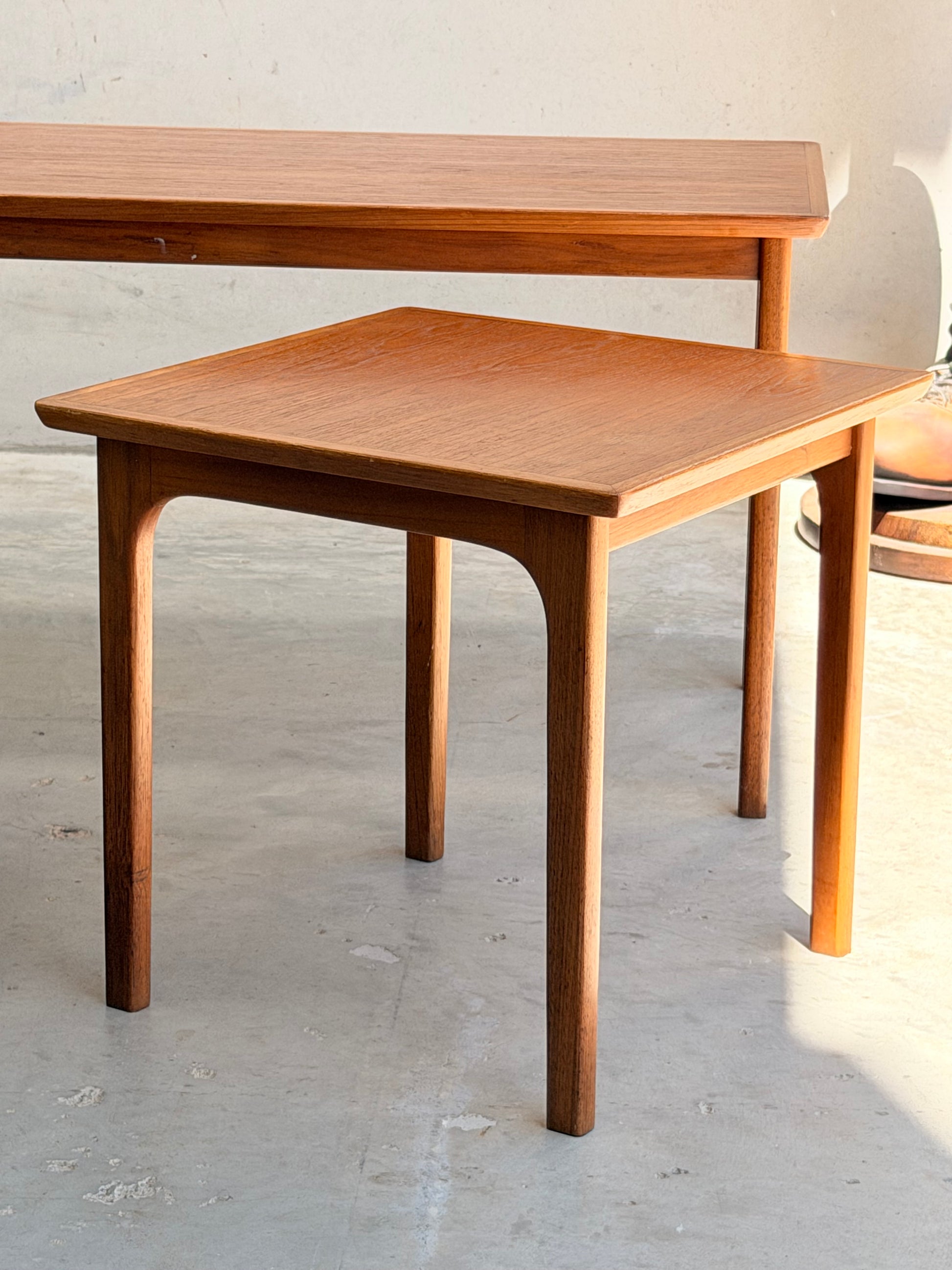 A set of Classic Australian-Made Noblett Mid-Century Teak Nesting Tables, circa 1970s, stands on a concrete floor in sunlight, their clean lines and warm wood reflecting timeless Scandinavian-inspired design.