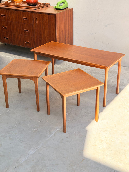 Three Classic Australian-Made Noblett Mid-Century Teak Nesting Tables – Circa 1970s (Revive) are set on a light concrete floor, with a Scandinavian-style wooden sideboard displaying a green rotary phone and decor in the background.