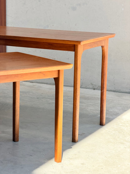 Two Classic Australian-Made Noblett Mid-Century Teak Nesting Tables – Circa 1970s (Revive) highlight timeless Scandinavian design, bathed in sunlight against a pale wall and casting gentle shadows across a concrete floor.