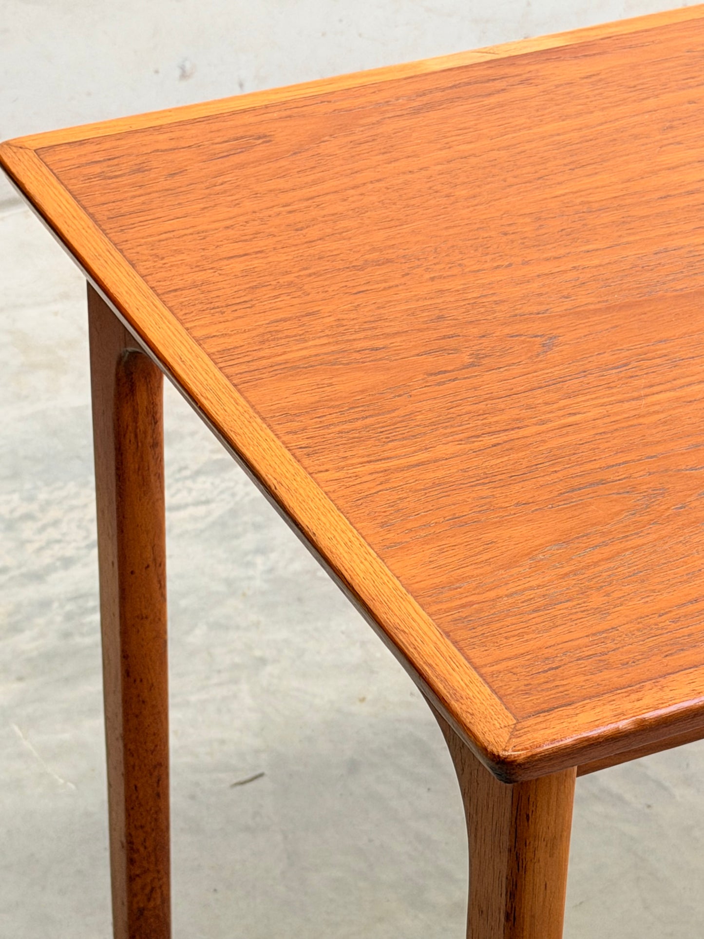 Close-up of the corner of a Classic Australian-Made Noblett Mid-Century Teak Nesting Table (Circa 1970s, Revive), featuring tapered legs and smooth teak grain inspired by Scandinavian design, standing on a light-colored floor.