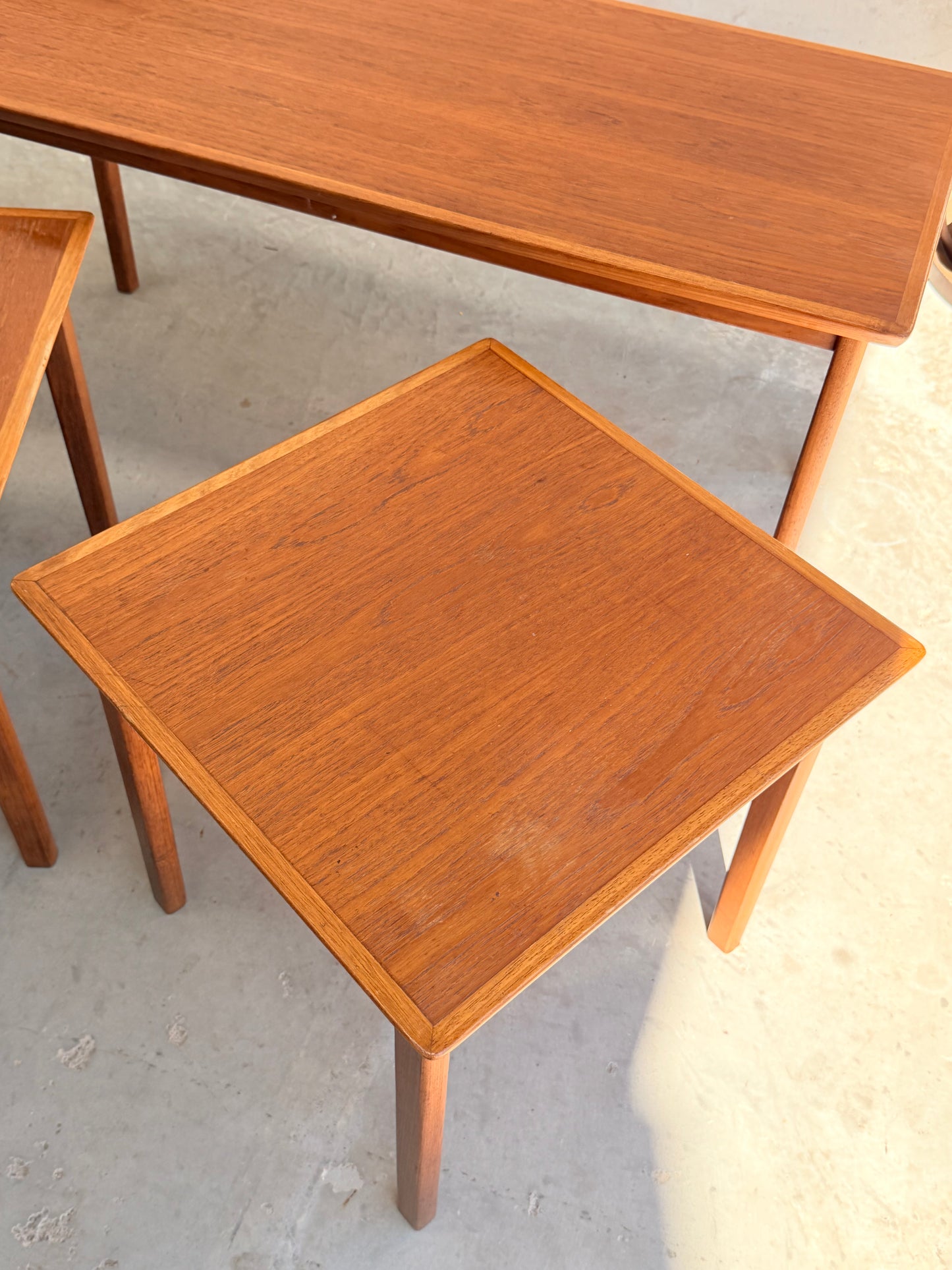 A square wooden side table with a smooth finish is shown beside Classic Australian-Made Noblett Mid-Century Teak Nesting Tables – Circa 1970s (Revive), all featuring simple, modern Scandinavian design with straight legs on a light floor.