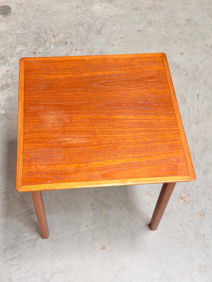 A Classic Australian-Made Noblett Mid-Century Teak Nesting Table from the 1970s, featuring a smooth, reddish-brown rectangular top and four legs, inspired by Scandinavian design, stands on a light gray concrete floor.