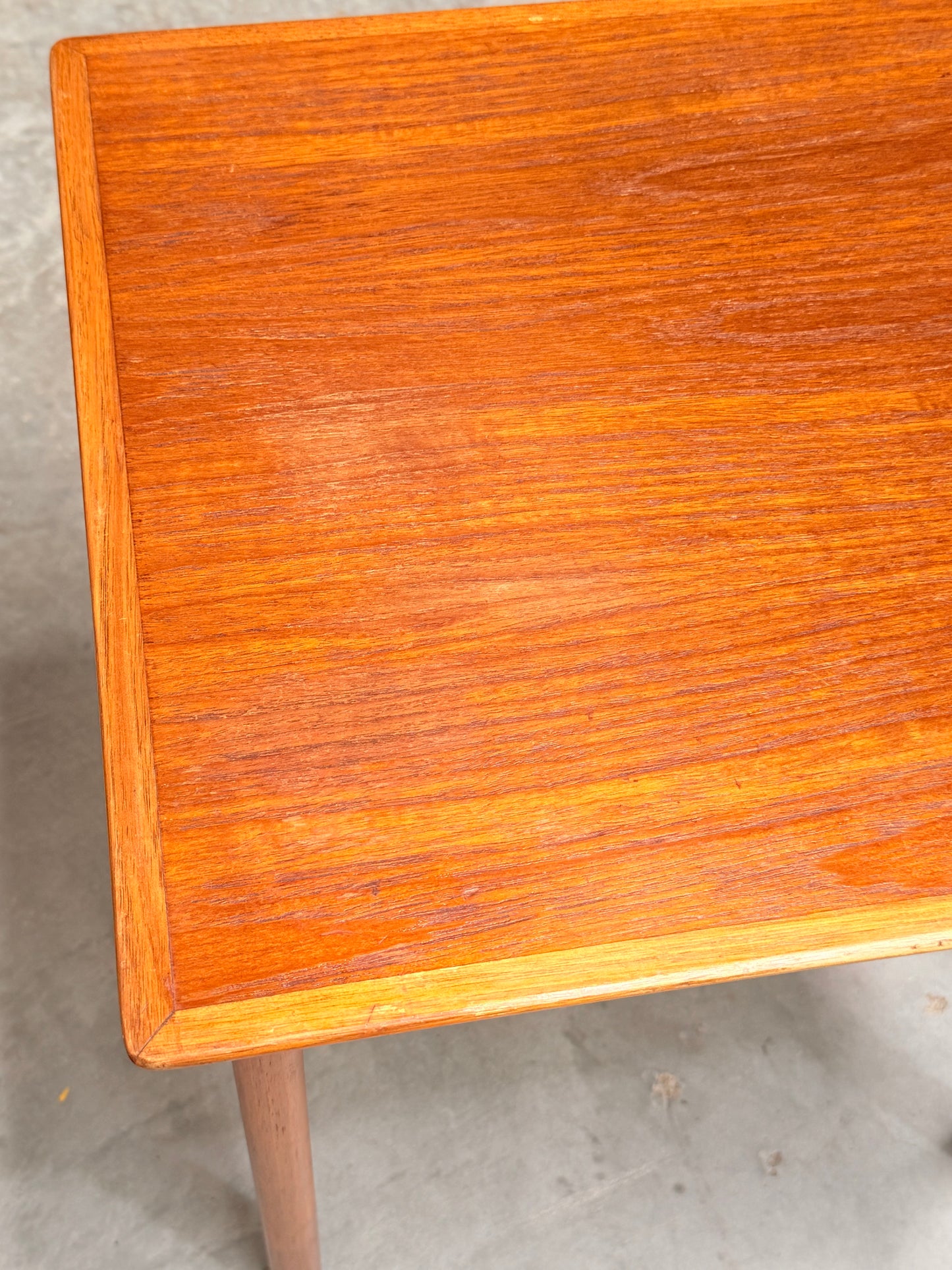 A close-up of the Classic Australian-Made Noblett Mid-Century Teak Nesting Tables – Circa 1970s (Revive), highlighting the corner and surface, set against a plain, light-colored floor.