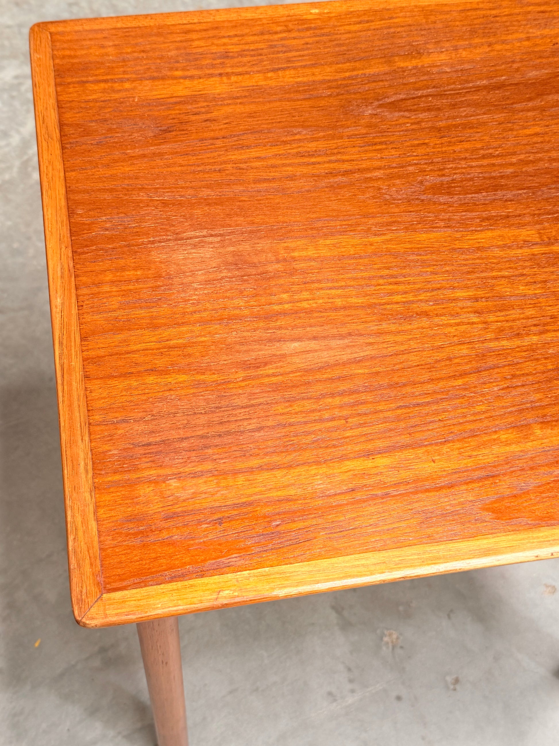 A close-up of the Classic Australian-Made Noblett Mid-Century Teak Nesting Tables – Circa 1970s (Revive), highlighting the corner and surface, set against a plain, light-colored floor.