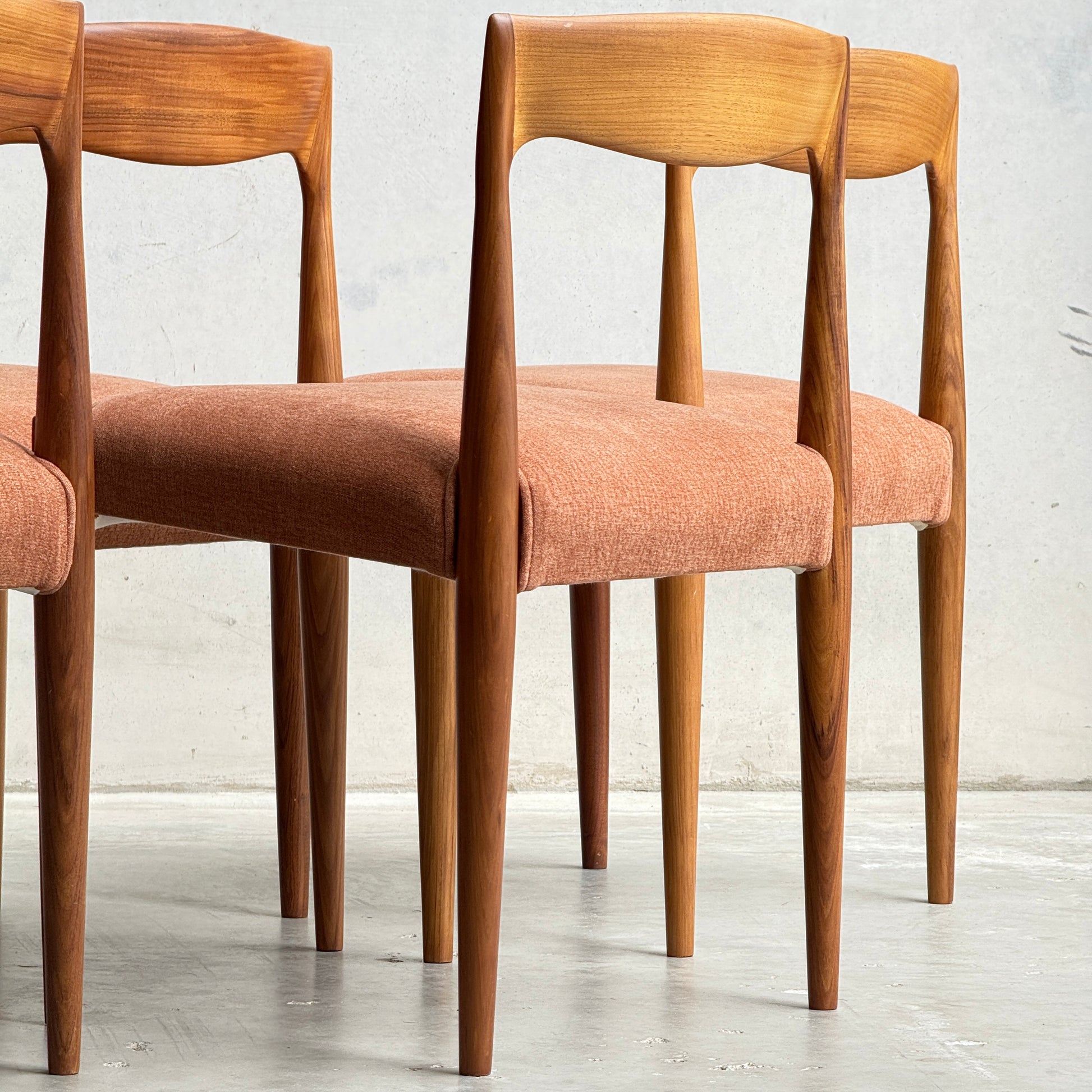 A set of four fully restored THB 'Milan' dining chairs from Rediscover, featuring curved backs and orange upholstered seats, are displayed in a row on a light floor against a plain light gray wall.