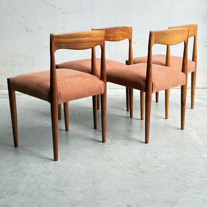 A set of four fully restored THB 'Milan' dining chairs from Rediscover, featuring Tasmanian blackwood and reddish-brown upholstered seats, are displayed in a staggered row on a concrete floor against a light gray wall.