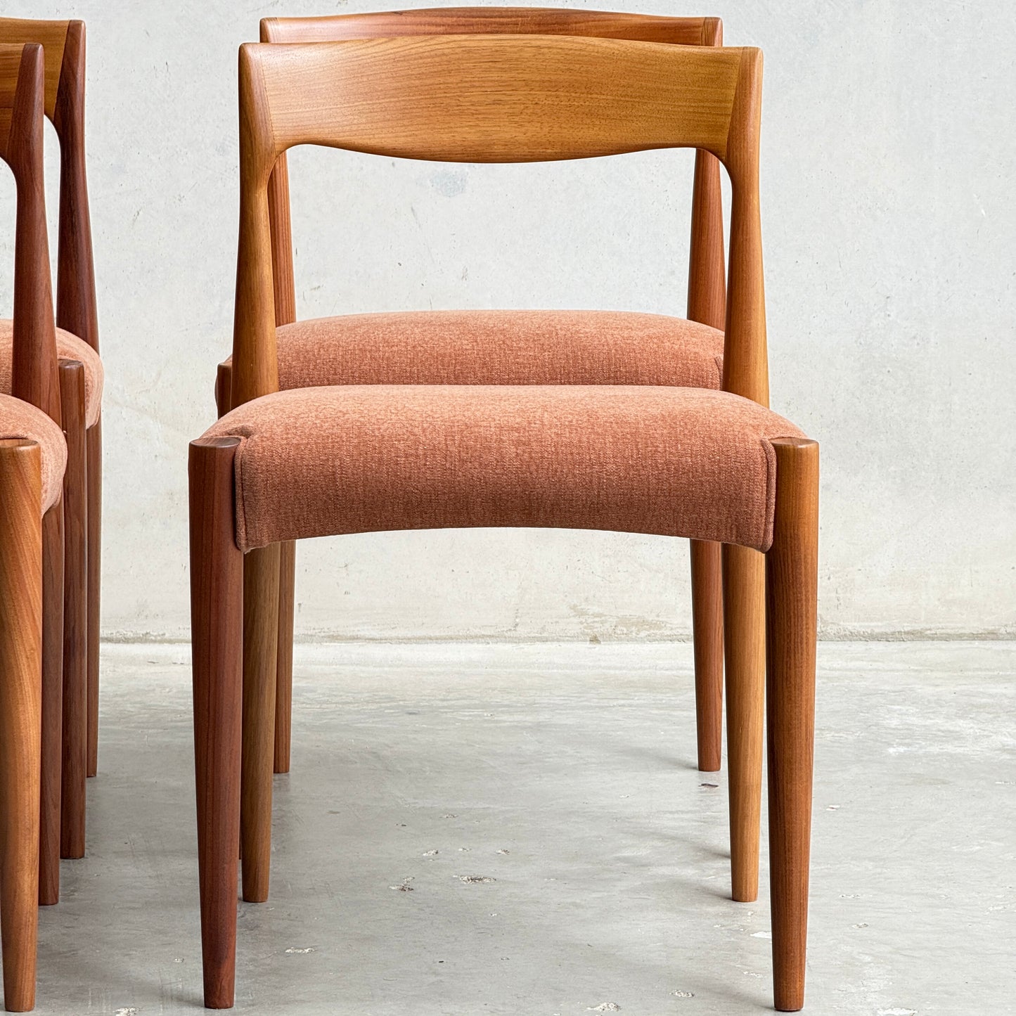 The Fully Restored THB 'Milan' Dining Chairs Set of 4 (Rediscover) includes wooden chairs with curved backrests, tapered legs, and rust-colored cushioned seats. Two similar chairs are partially visible beside it against a plain light wall.