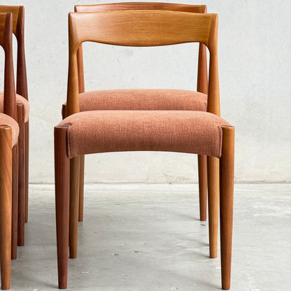 The Fully Restored THB 'Milan' Dining Chairs Set of 4 (Rediscover) includes wooden chairs with curved backrests, tapered legs, and rust-colored cushioned seats. Two similar chairs are partially visible beside it against a plain light wall.