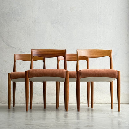 A set of four fully restored THB 'Milan' dining chairs (Rediscover), featuring minimalist mid-century modern design, is arranged in a staggered row against a plain light gray wall. Each chair has curved backrests and light brown upholstered seats.