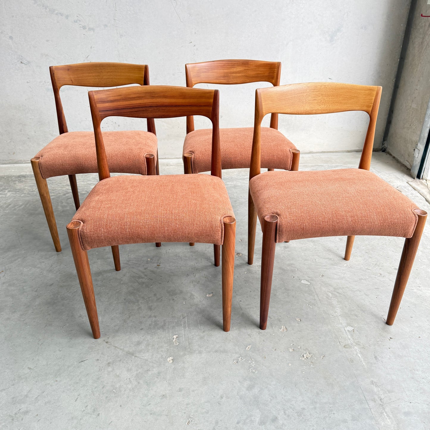 A set of four fully restored THB 'Milan' dining chairs (Rediscover), crafted from Tasmanian blackwood with curved backs and muted orange upholstered seats, arranged in two rows on a concrete floor against a plain wall.
