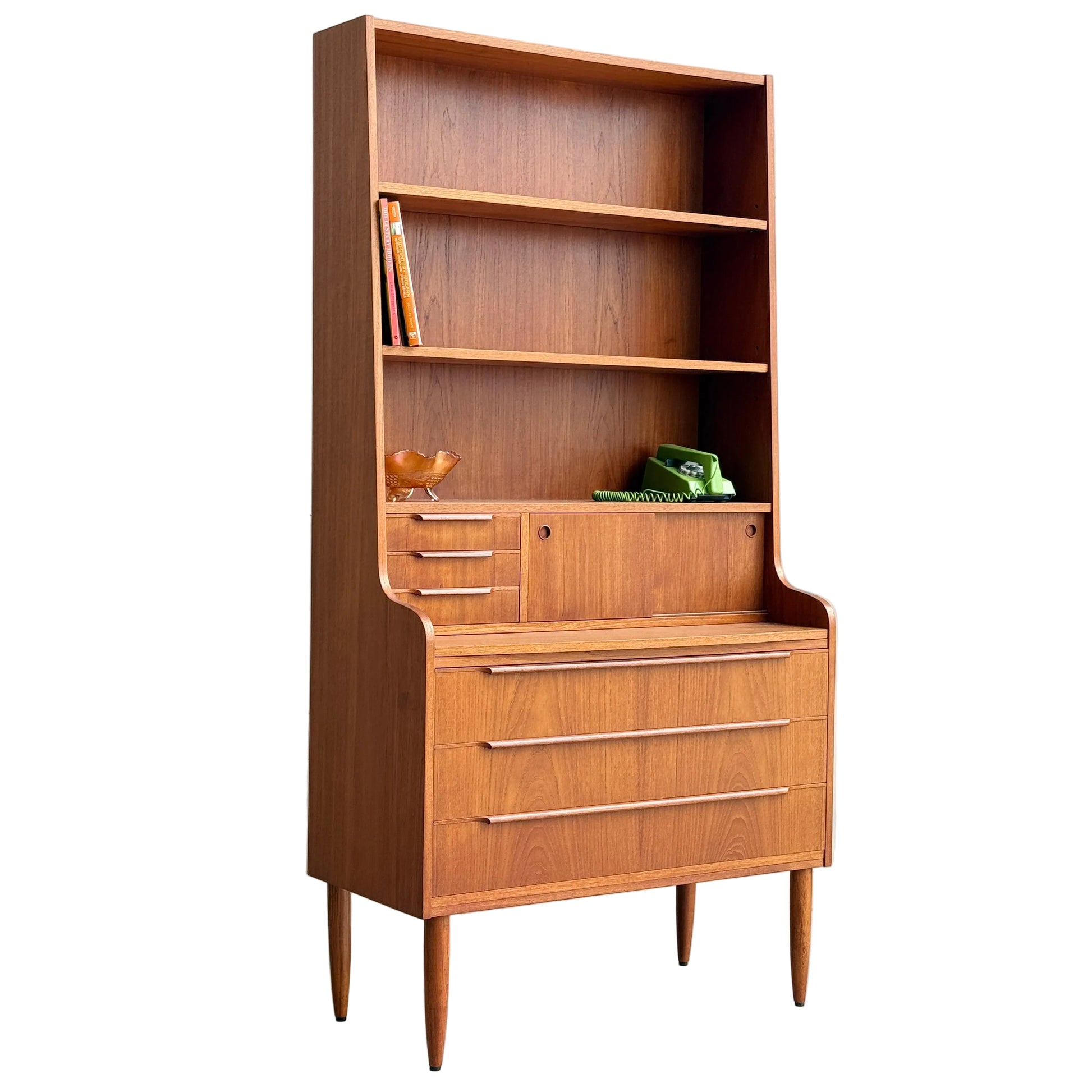 A mid-century Danish teak bureau bookcase secretary desk by Erik Petersen for EP Møbler featuring three large drawers, a writing surface, upper shelves with books, a wooden bird, and a green rotary phone—all on classic tapered Scandinavian legs.