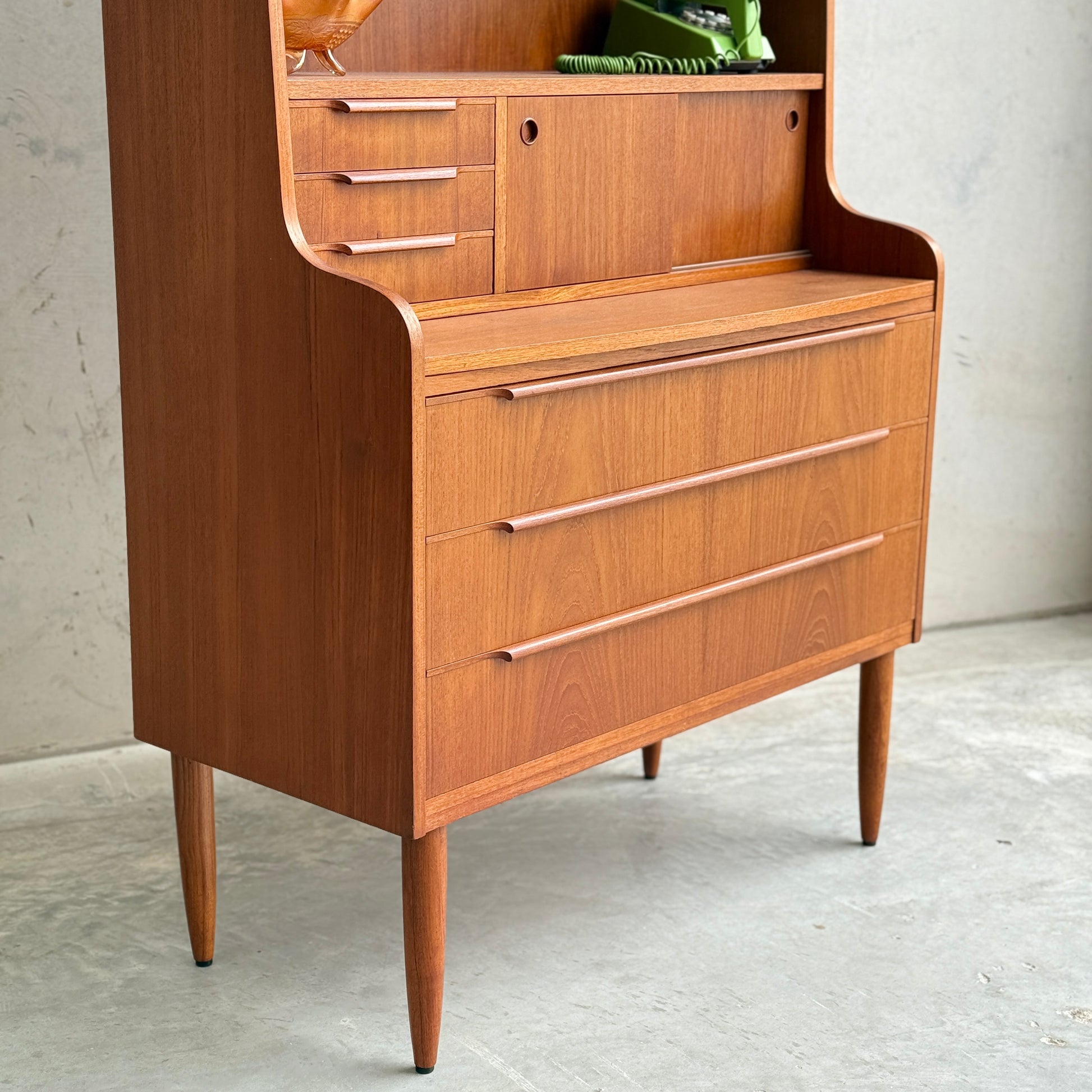 The Danish Teak Bureau Bookcase Secretary Desk by Erik Petersen for EP Møbler features mid-century modern design with curved edges, three wide drawers, an open shelf with small drawers and a cubby, set on four tapered legs.