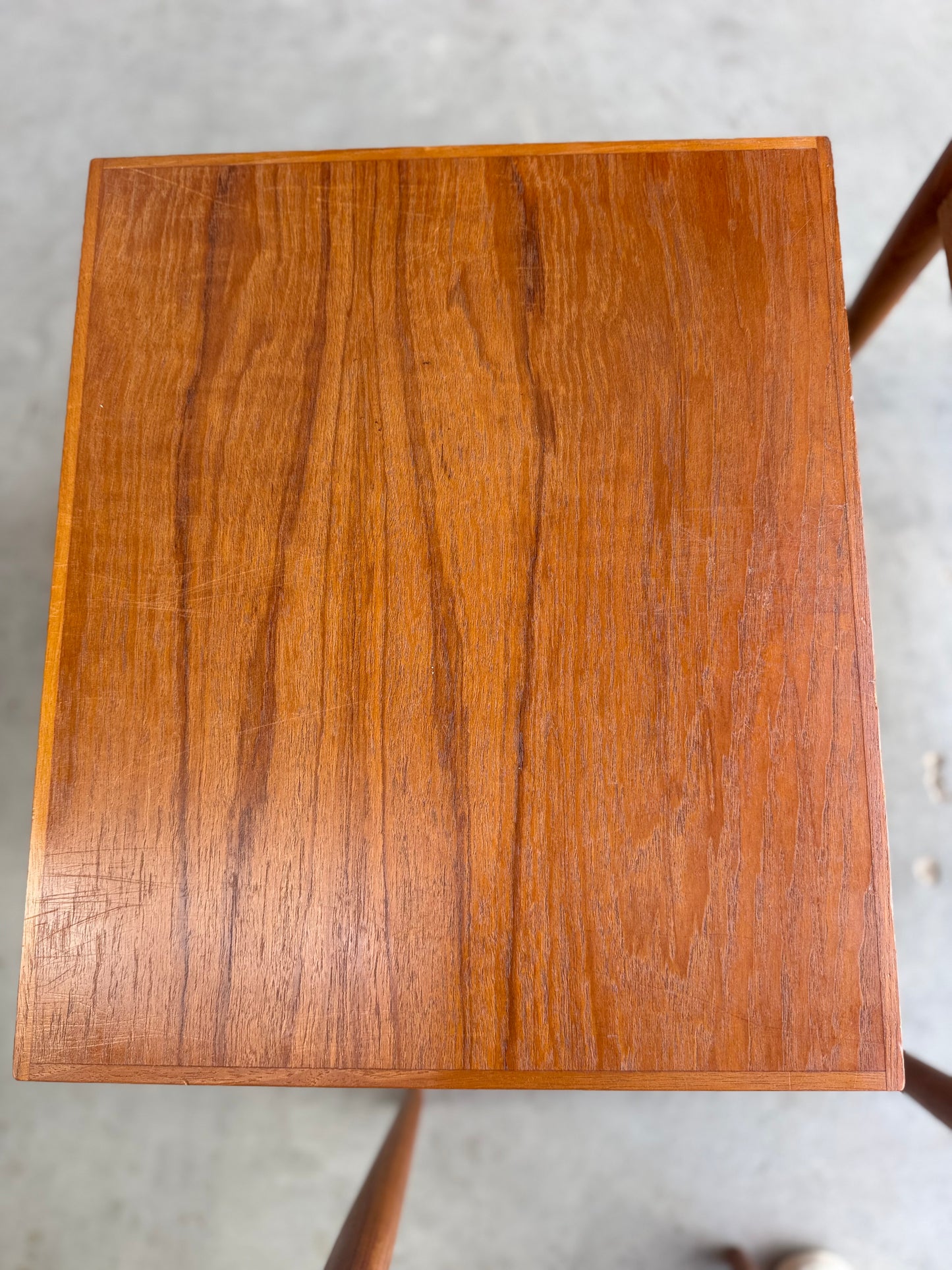 A close-up view of Noblett Mid-Century Floating Teak Nesting Tables – Circa 1960s (Revive) shows their rich brown finish, visible grain patterns, and classic Danish-inspired design on a light gray floor.