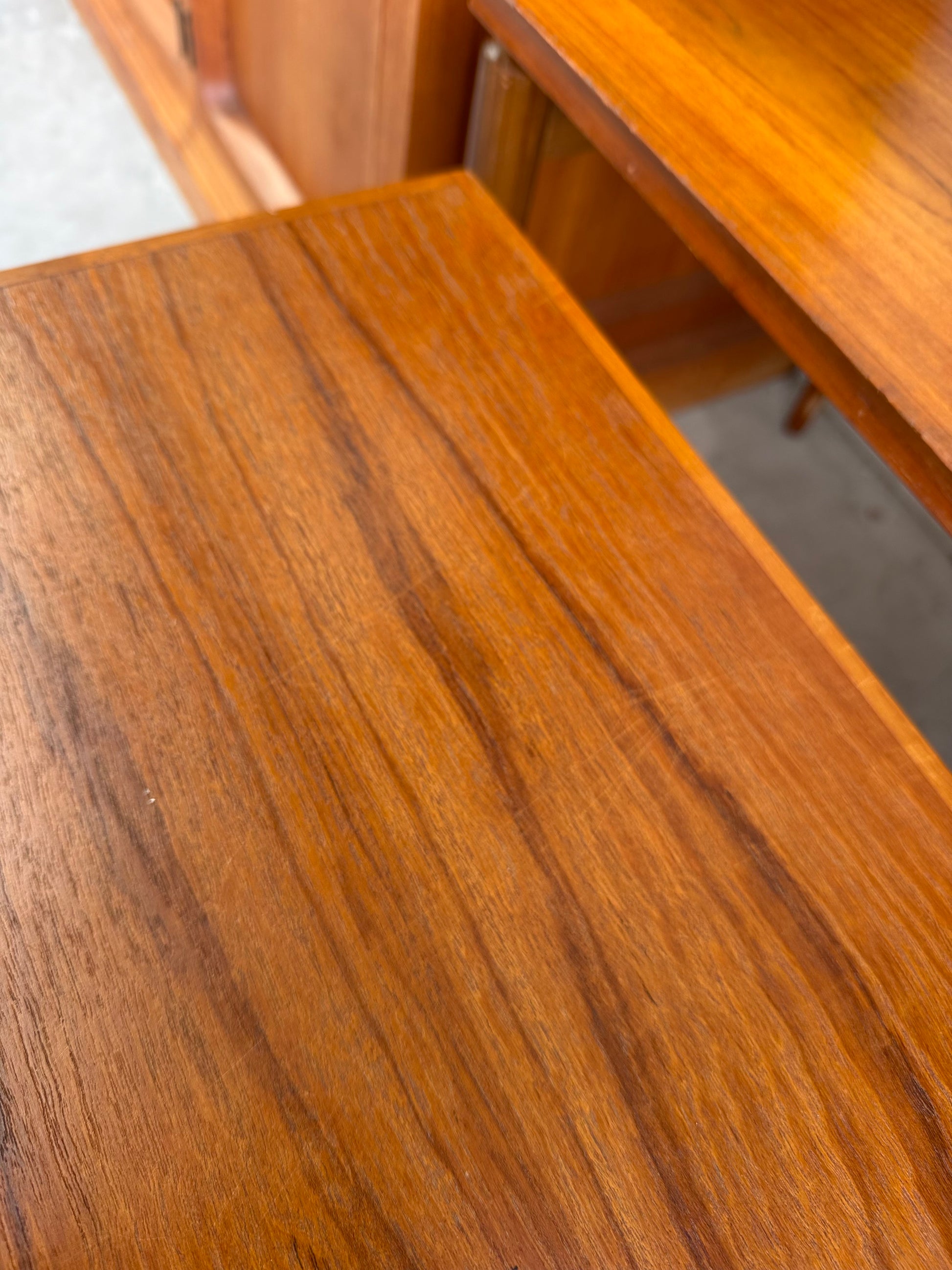 Close-up of a teak surface with natural brown grain and smooth finish. In the background is another Noblett Mid-Century Floating Teak Nesting Table – Circa 1960s (Revive).