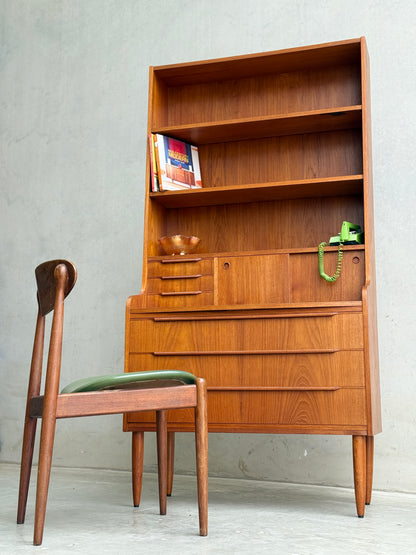A Danish Teak Bureau Bookcase Secretary Desk by Erik Petersen for EP Møbler, paired with a matching wooden chair featuring a green cushion, plus a green rotary phone and books, set before a plain concrete wall.