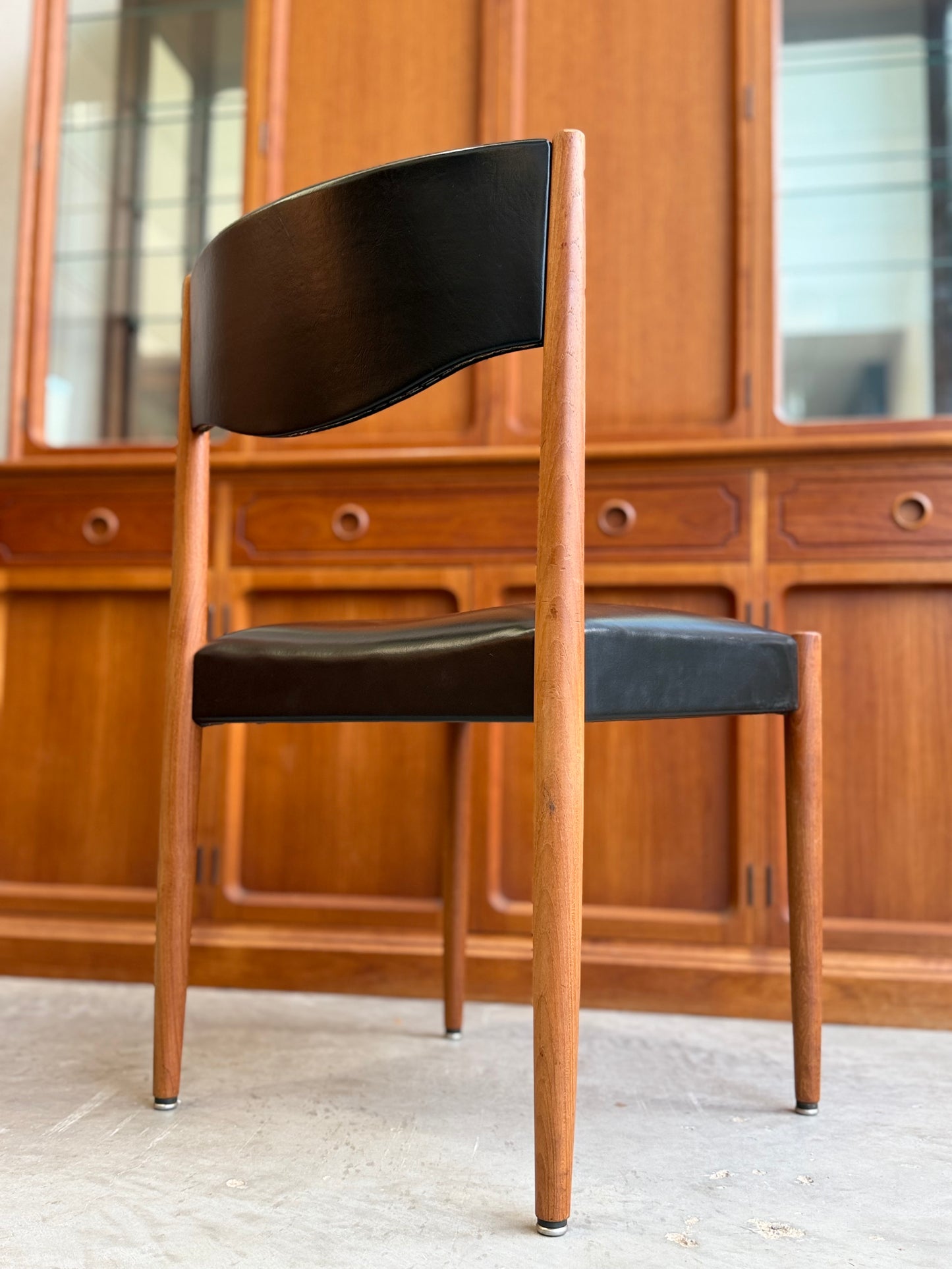 Teak Parker number 62 chair with black seat and backrest in front of wooden cabinets.