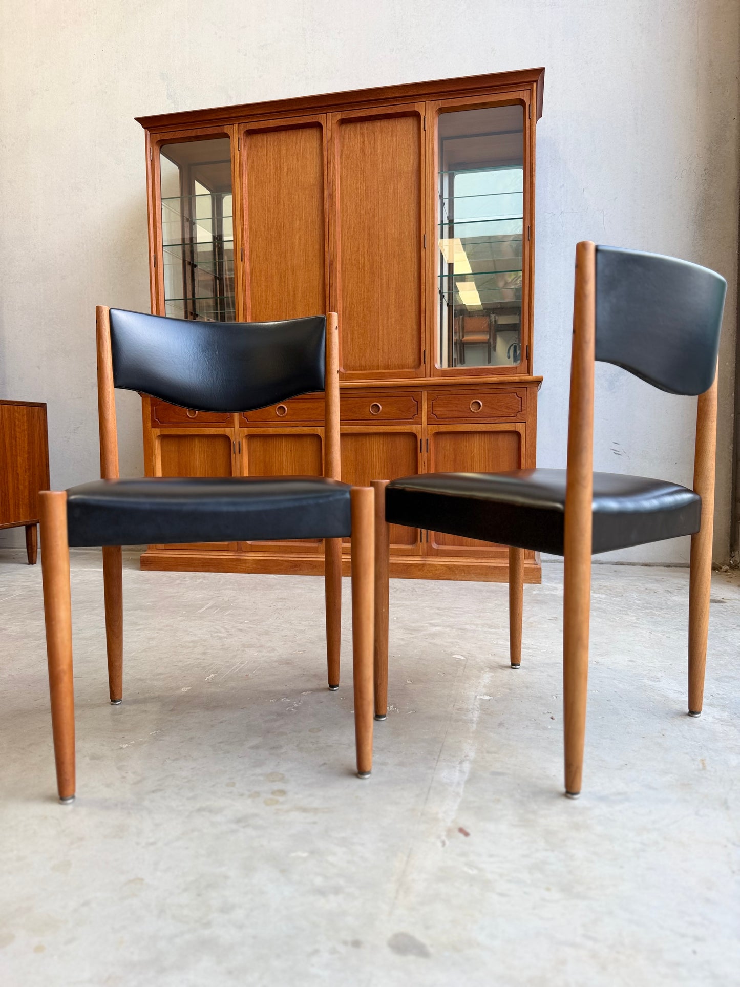 Two Parker 62 chairs in orginal black leather chairs with wooden frames in front of a wooden cabinet.