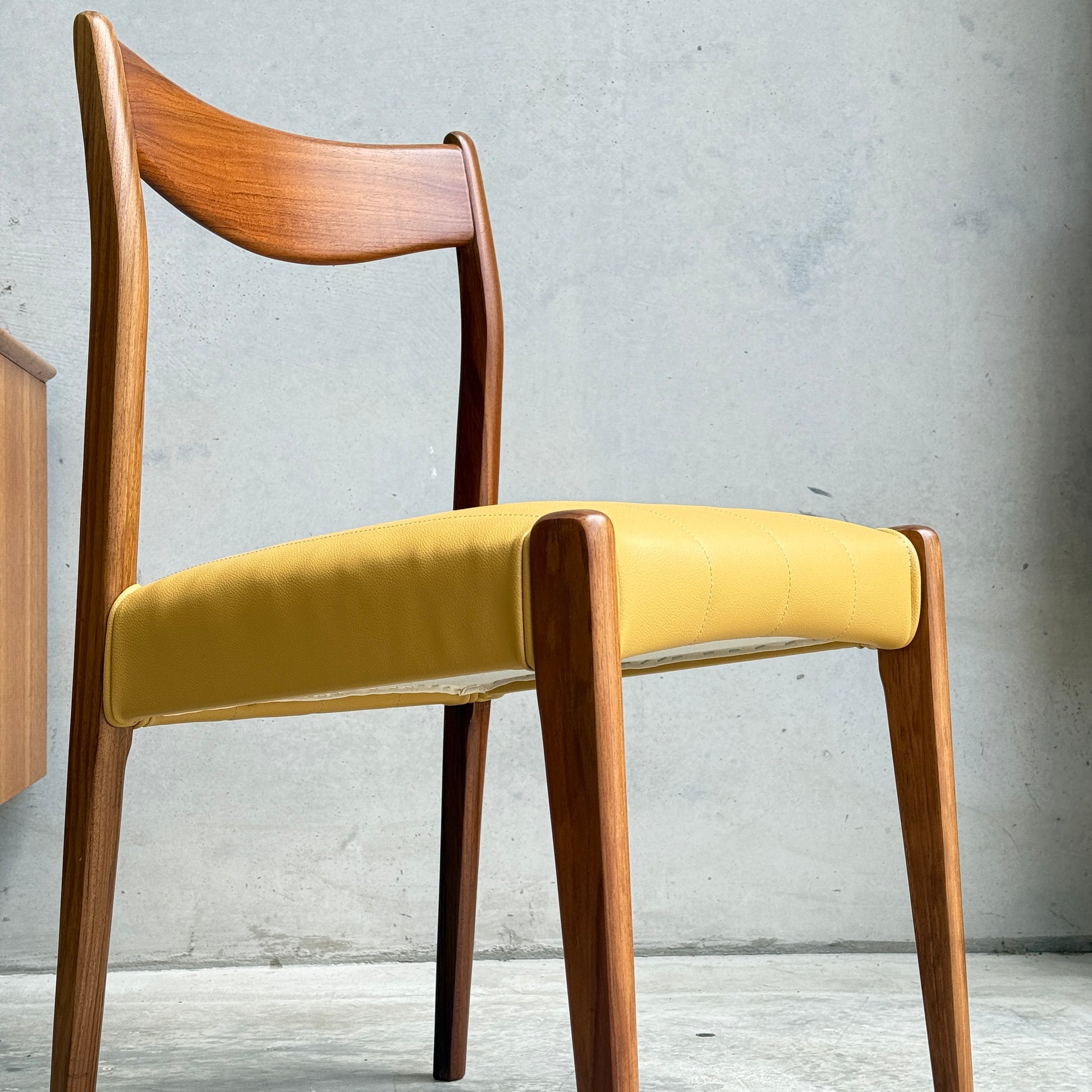 A set of fully restored THB 'Stockholm' dining chairs, featuring curved backrests and yellow upholstered seats, stands against a plain light-colored concrete wall.