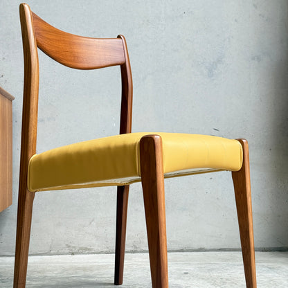 A set of fully restored THB 'Stockholm' dining chairs, featuring curved backrests and yellow upholstered seats, stands against a plain light-colored concrete wall.