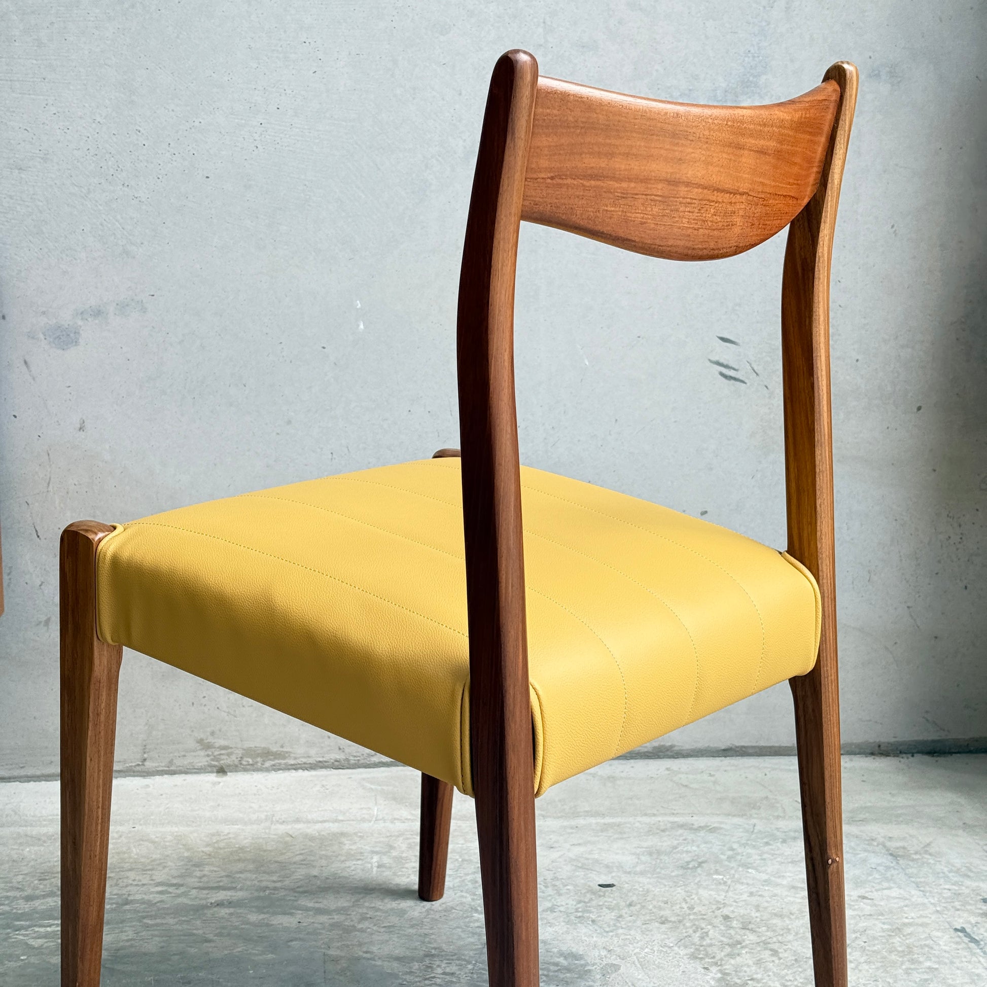 A set of four fully restored THB 'Stockholm' dining chairs is displayed, each with a curved backrest, elegant legs, and padded yellow seat, set on concrete flooring against a plain gray wall.
