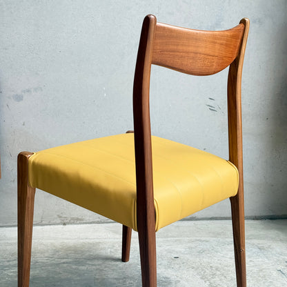 A set of four fully restored THB 'Stockholm' dining chairs is displayed, each with a curved backrest, elegant legs, and padded yellow seat, set on concrete flooring against a plain gray wall.