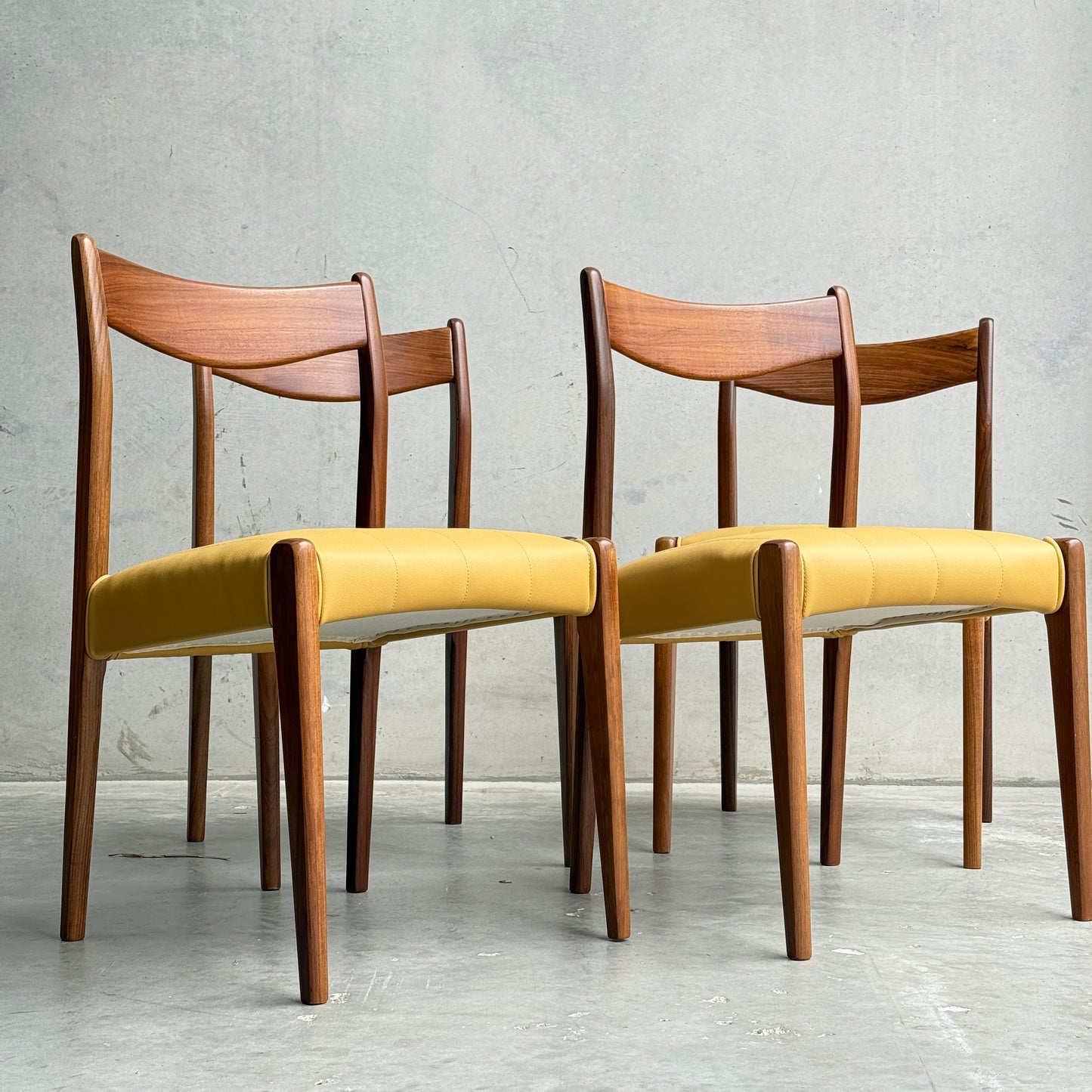 Two fully restored THB 'Stockholm' dining chairs from a set of 4, featuring curved backrests and yellow upholstered seats, are placed side by side on a concrete floor against a plain light gray wall.