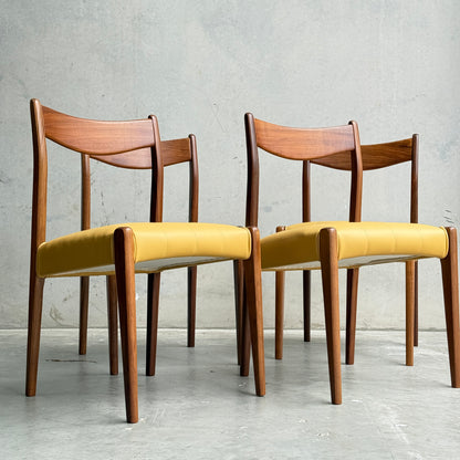 Two fully restored THB 'Stockholm' dining chairs from a set of 4, featuring curved backrests and yellow upholstered seats, are placed side by side on a concrete floor against a plain light gray wall.