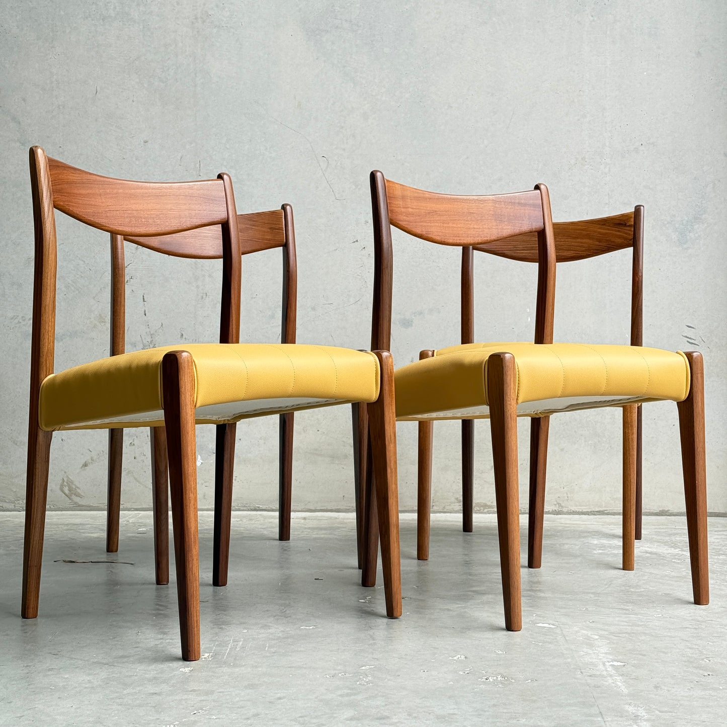 A set of four fully restored THB 'Stockholm' dining chairs with curved backs, angled legs, and mustard yellow upholstered seats in Tasmanian blackwood sit on a concrete floor against a plain gray wall.