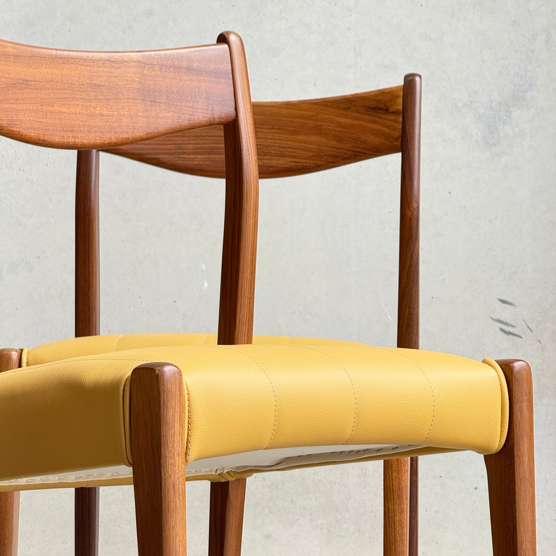 A set of four fully restored THB 'Stockholm' dining chairs (Rediscover) with curved backrests and mustard yellow cushions are stacked against a light gray wall.