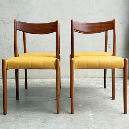 Two fully restored THB 'Stockholm' dining chairs (set of 4) with curved backrests and mustard yellow seats stand side by side on a concrete floor against a plain gray wall.