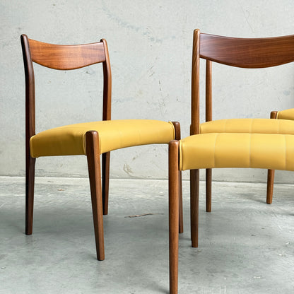 A set of four fully restored THB 'Stockholm' dining chairs, featuring curved backs and mustard yellow seats, is showcased on a concrete floor against a textured gray wall.