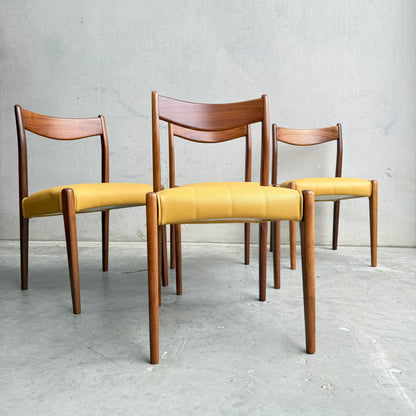 A set of four fully restored THB 'Stockholm' dining chairs with Tasmanian blackwood frames and mustard yellow upholstery, arranged on a gray concrete floor against a plain light gray wall.